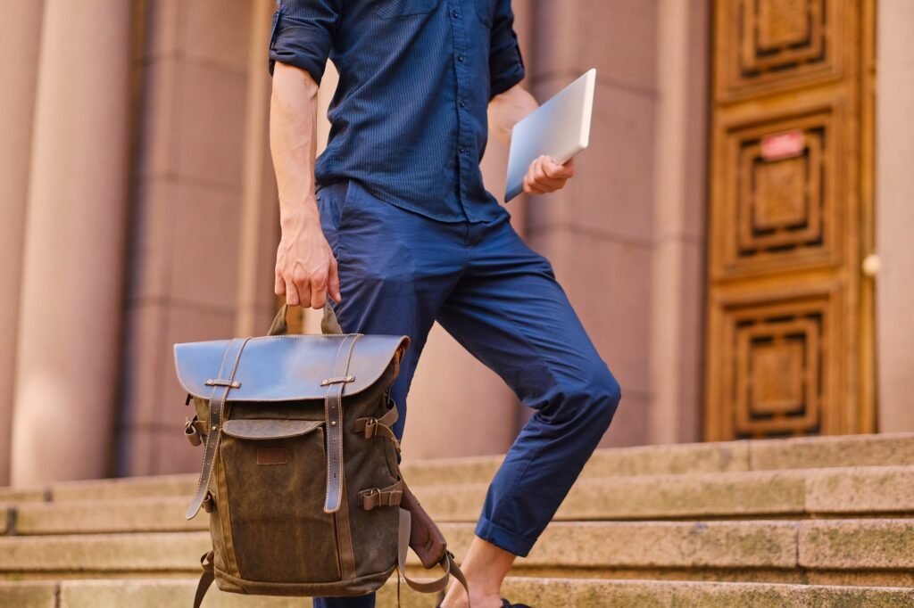 A man holds leather backpack and tablet PC.