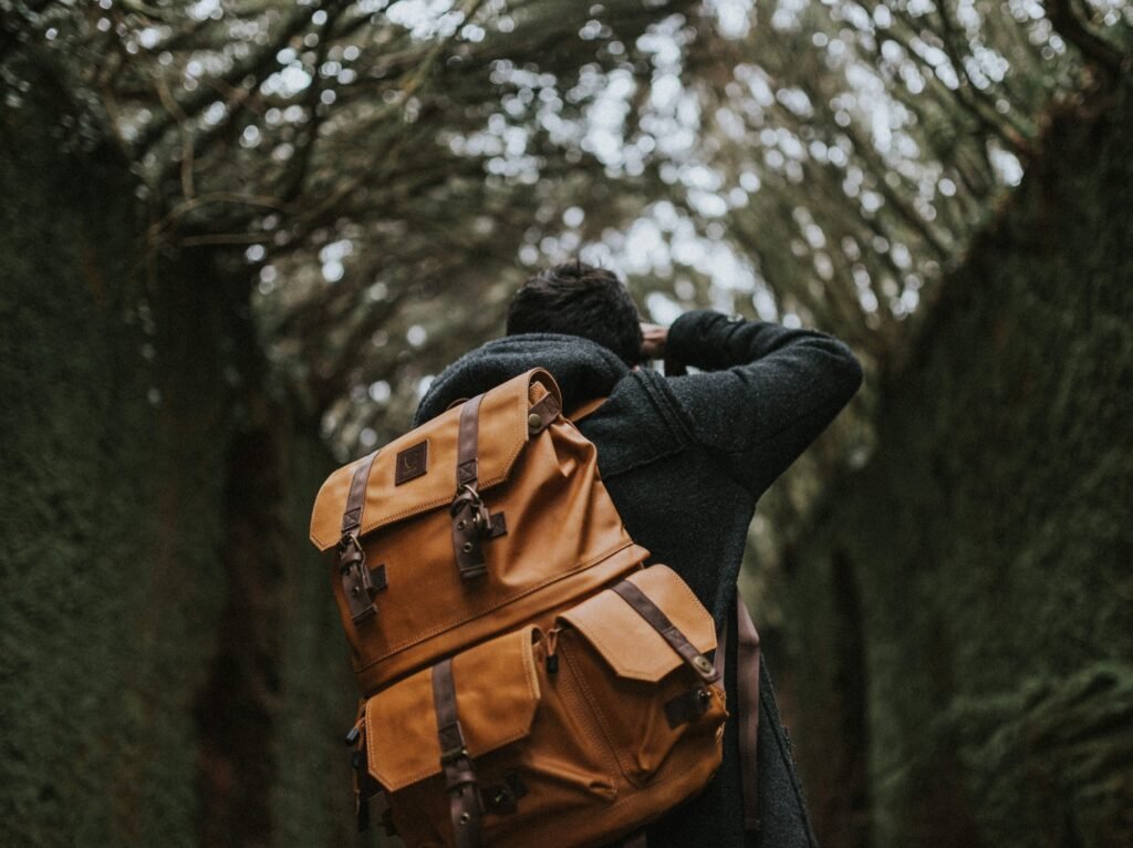 A photographer’s back with a leather backpack taking a picture in nature