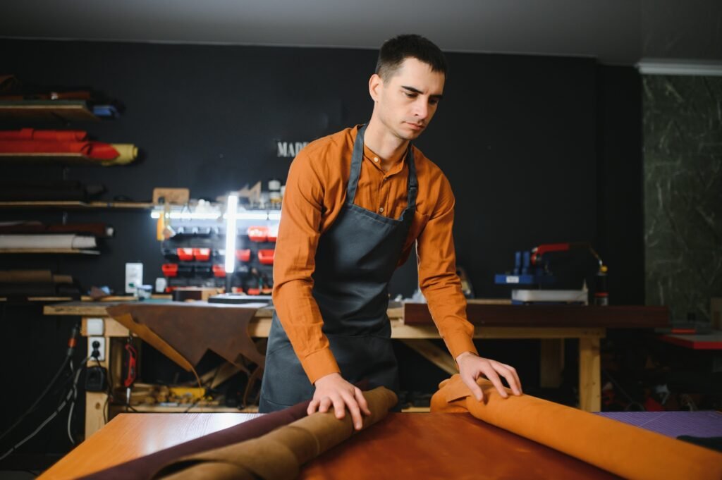 Production process. Young focused experienced master craftsman makes leather goods at his workplace